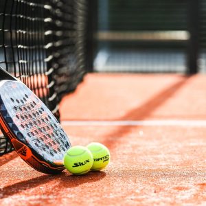 Photograph of padel racket and two padel balls resting against net on padel courts, close up photo.