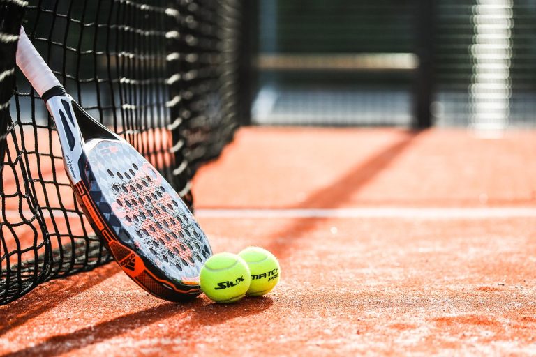 Photograph of padel racket and two padel balls resting against net on padel courts, close up photo.